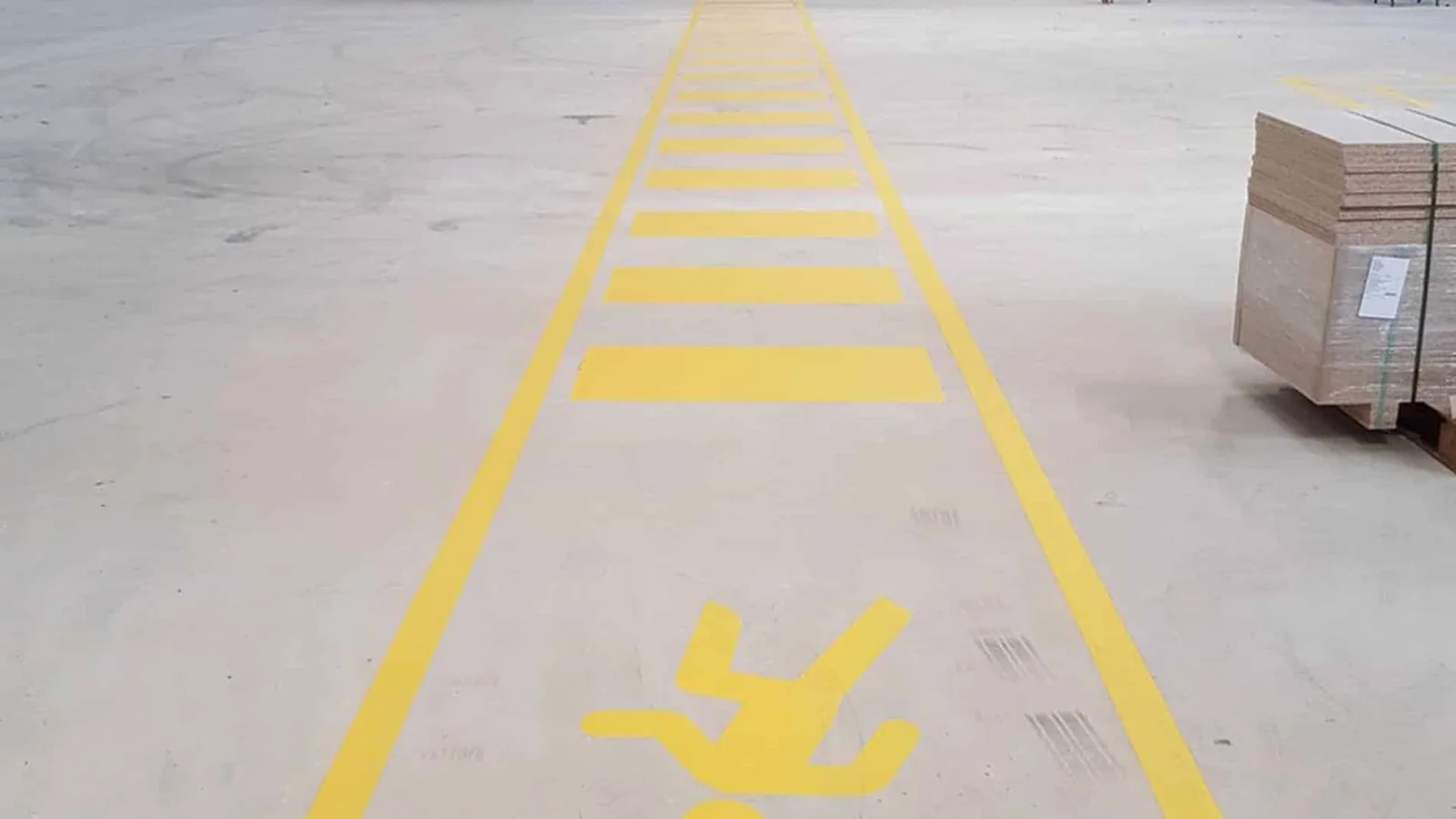 A yellow walk path warehouse line marking on a grey concrete floor inside.