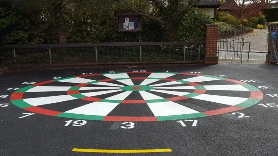 A green, red, black and white dartboard that has been painted on new tarmac in a gated area.